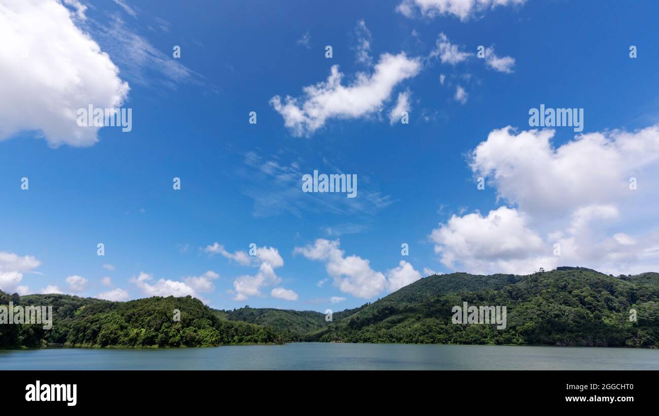 White clouds in blue sky over green mountains covered with rainforests trees Beautiful landscape of Mountain and Lake with reflex in the water scenery Stock Photo