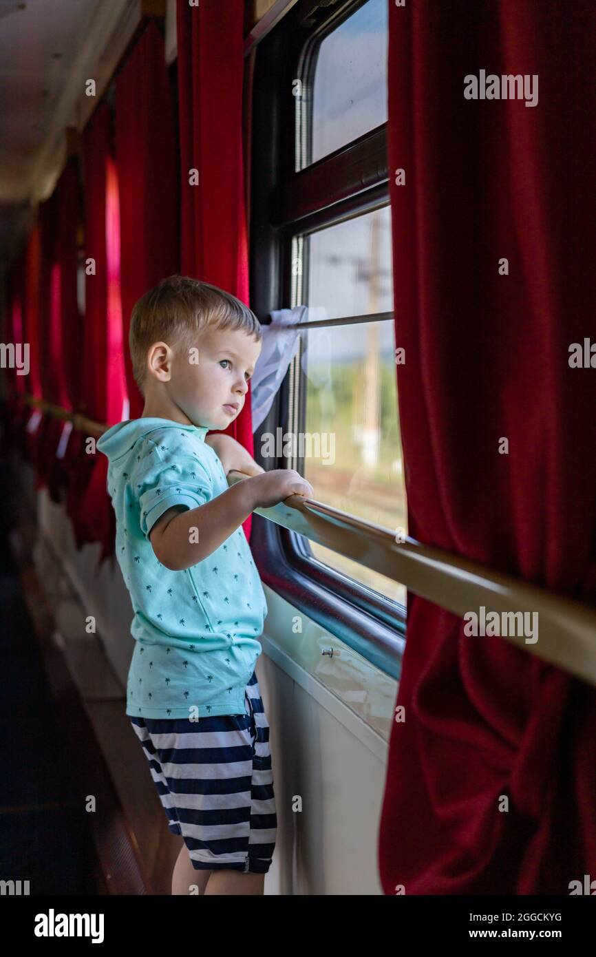 Pensive little boy looking through window traveling by train at