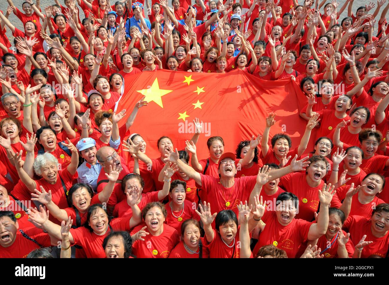 Local Chinese citizens surrounding the Chinese national flag laugh during a laughing campaign to celebrate the upcoming National Day, marking the 60th Stock Photo