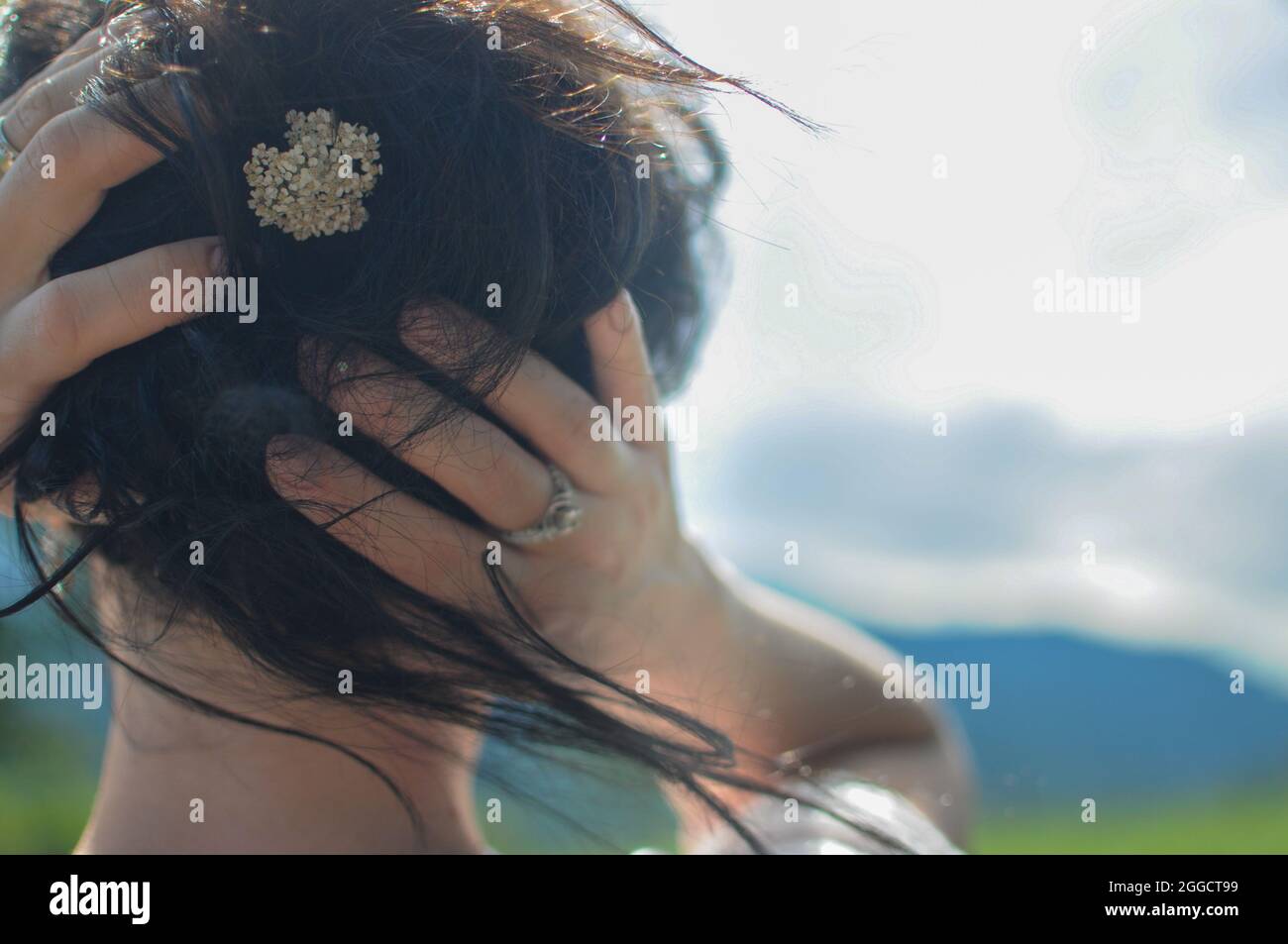 A girl is holding her hair with the little flower in her hand. Natural hairstyle Stock Photo