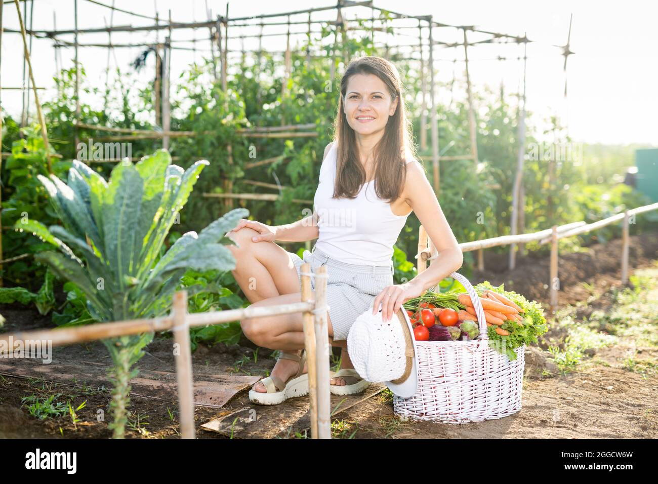 Happy smiling woman with basket of vegetables in the summer garden ...