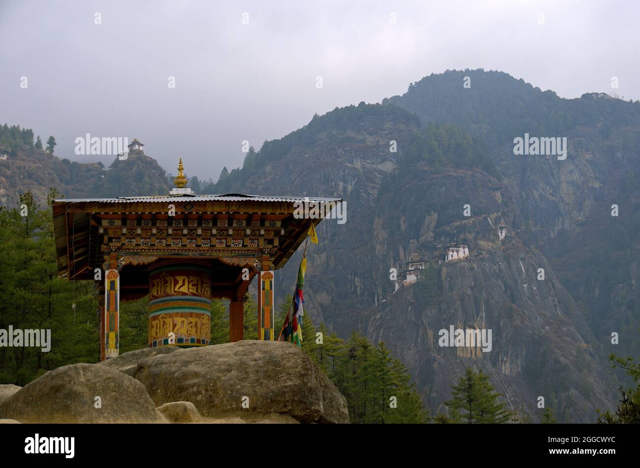 Large Tibetan 'Mani' Prayer Wheel along trail to Paro Taktsang or Tiger's Nest Buddhist Monastery, with the temple complex in the background, Bhutan Stock Photo