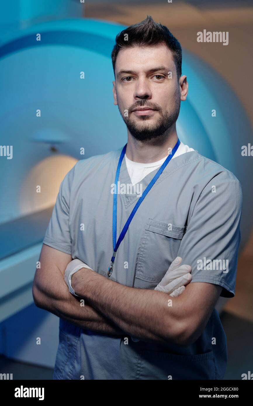 Young successful doctor in uniform standing against medical equipment