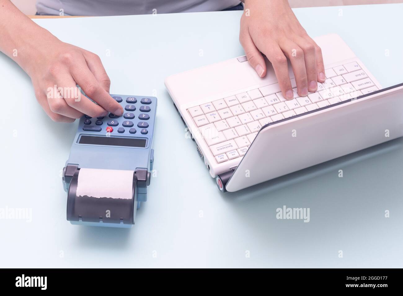 Hand typing on a laptop and a cash register on a blue background. Sales person entering amount on cash register in retail store. Online e-commerce sho Stock Photo