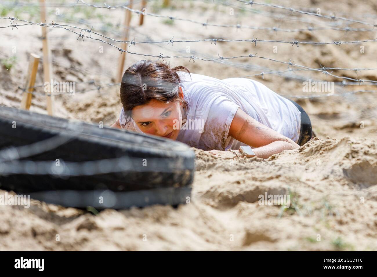 Young sportswoman crawling under barbed wire on her obstacle race course Stock Photo