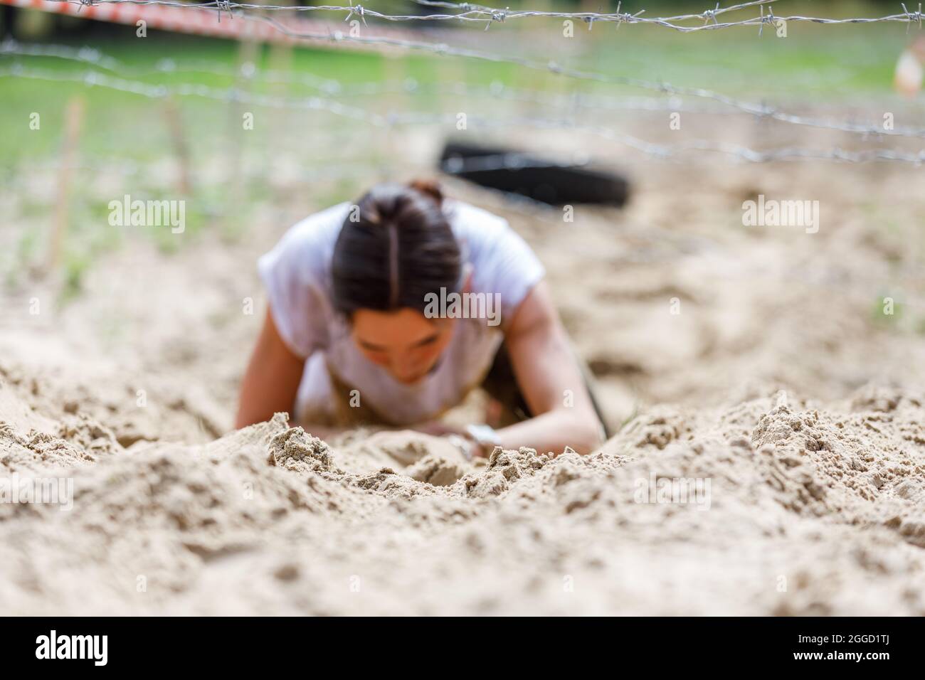 Young sportswoman crawling under barbed wire on her obstacle race course Stock Photo