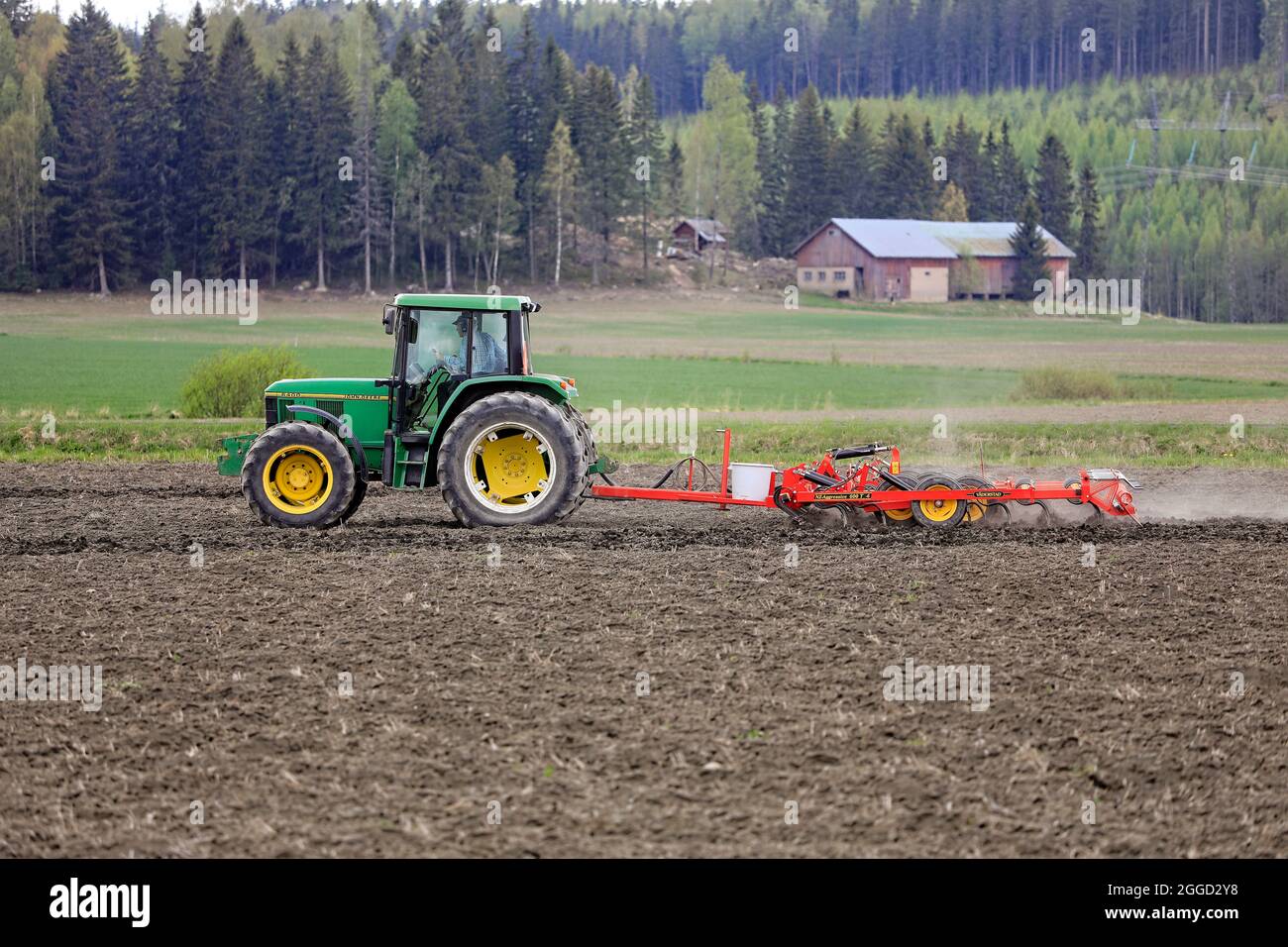Farmer cultivating field with green John Deere 6400 tractor and harrow in the spring. Salo, Finland. May 15, 2021. Stock Photo