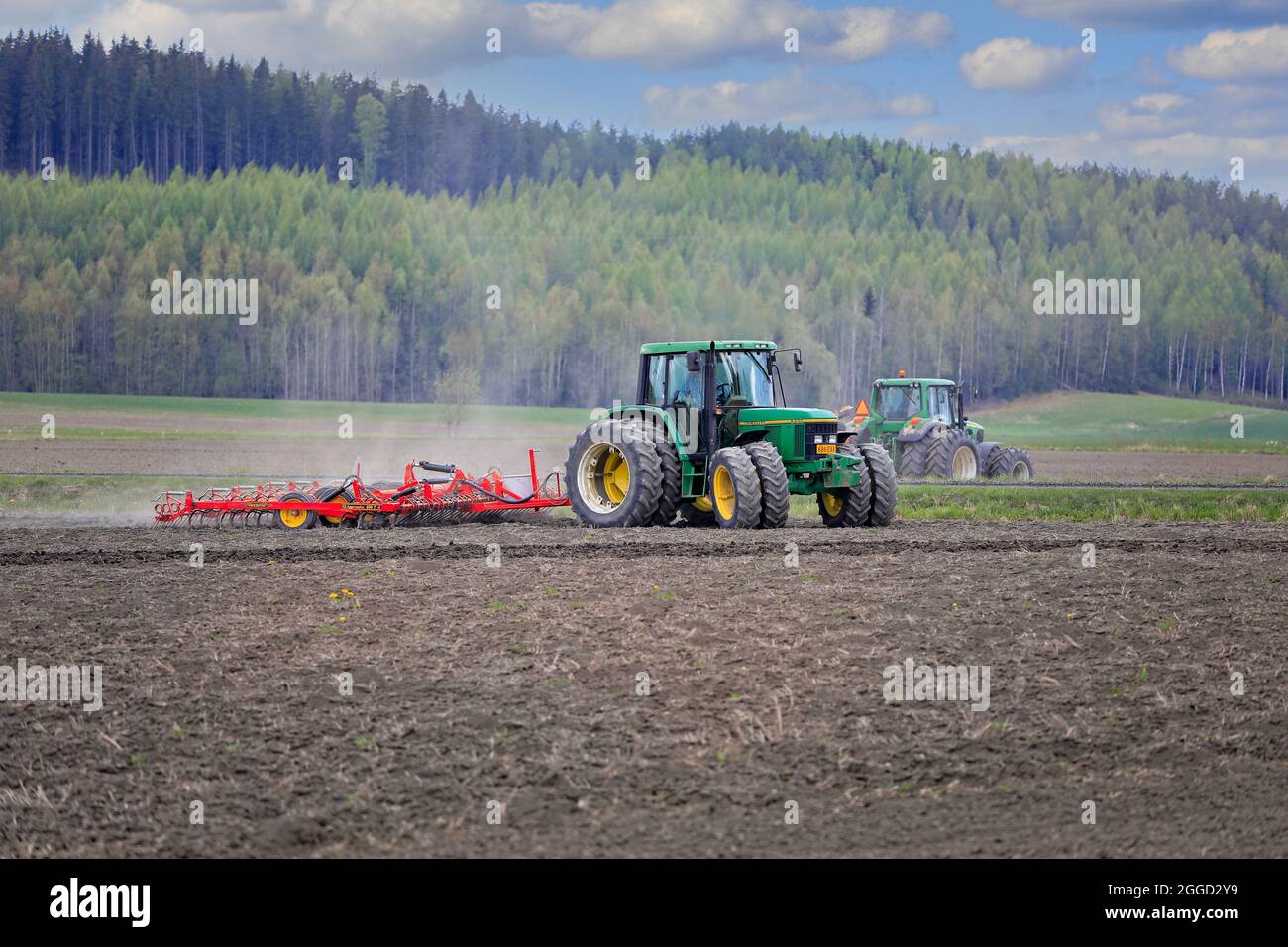 Farmer cultivating field with green John Deere 6520 tractor and Vaderstad harrow, another tractor on the background. Salo, Finland. May 15, 2021. Stock Photo