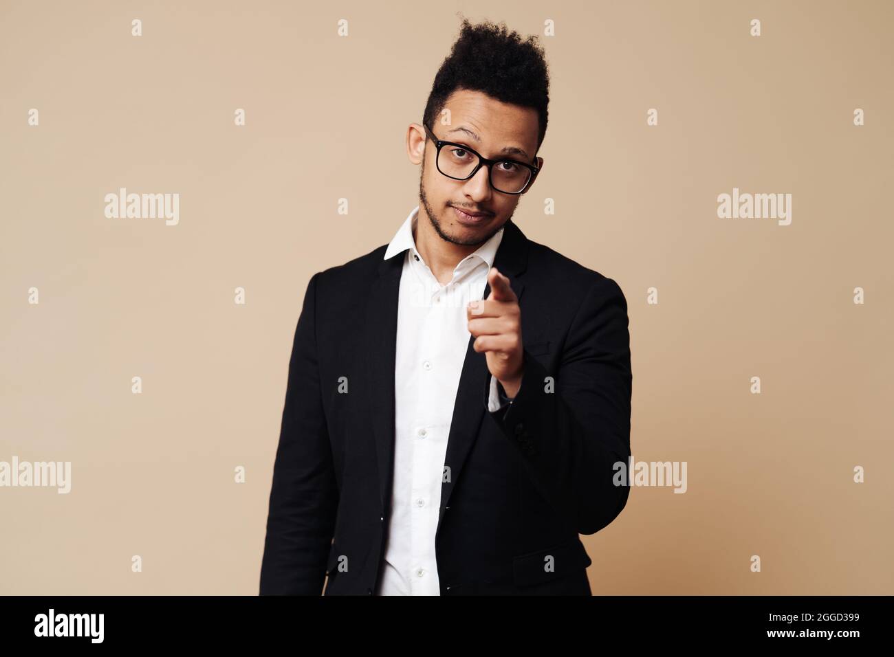 Portrait of a confident young Afro businessman dressed in suit pointing finger at camera isolated over beige background with copy space Stock Photo