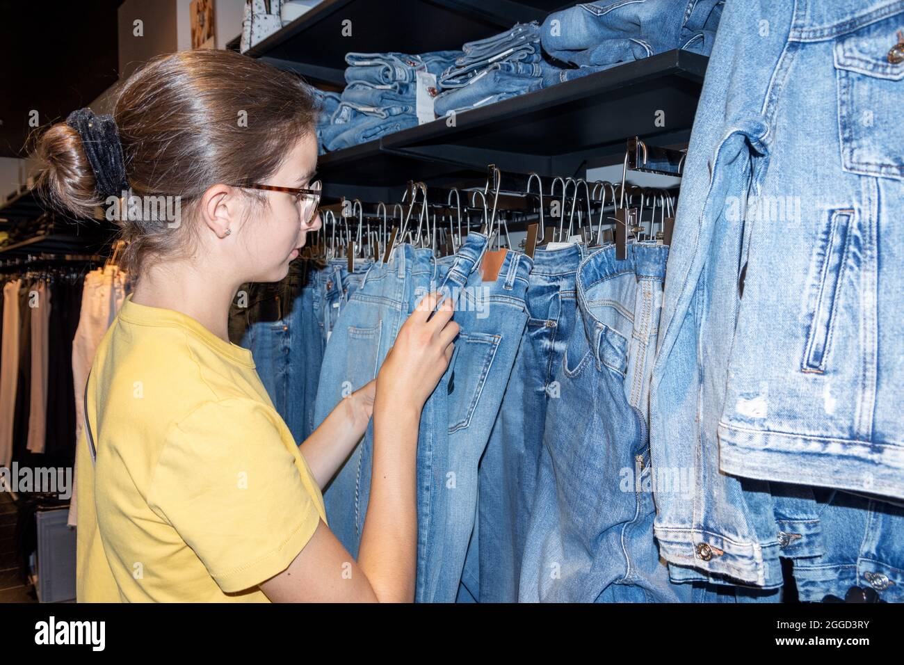 Girl choosing jeans jacket hanging on hangers in a boutique. Reasonable consumption concept. Sale of clothes in stores and online concept. Seasonal sa Stock Photo