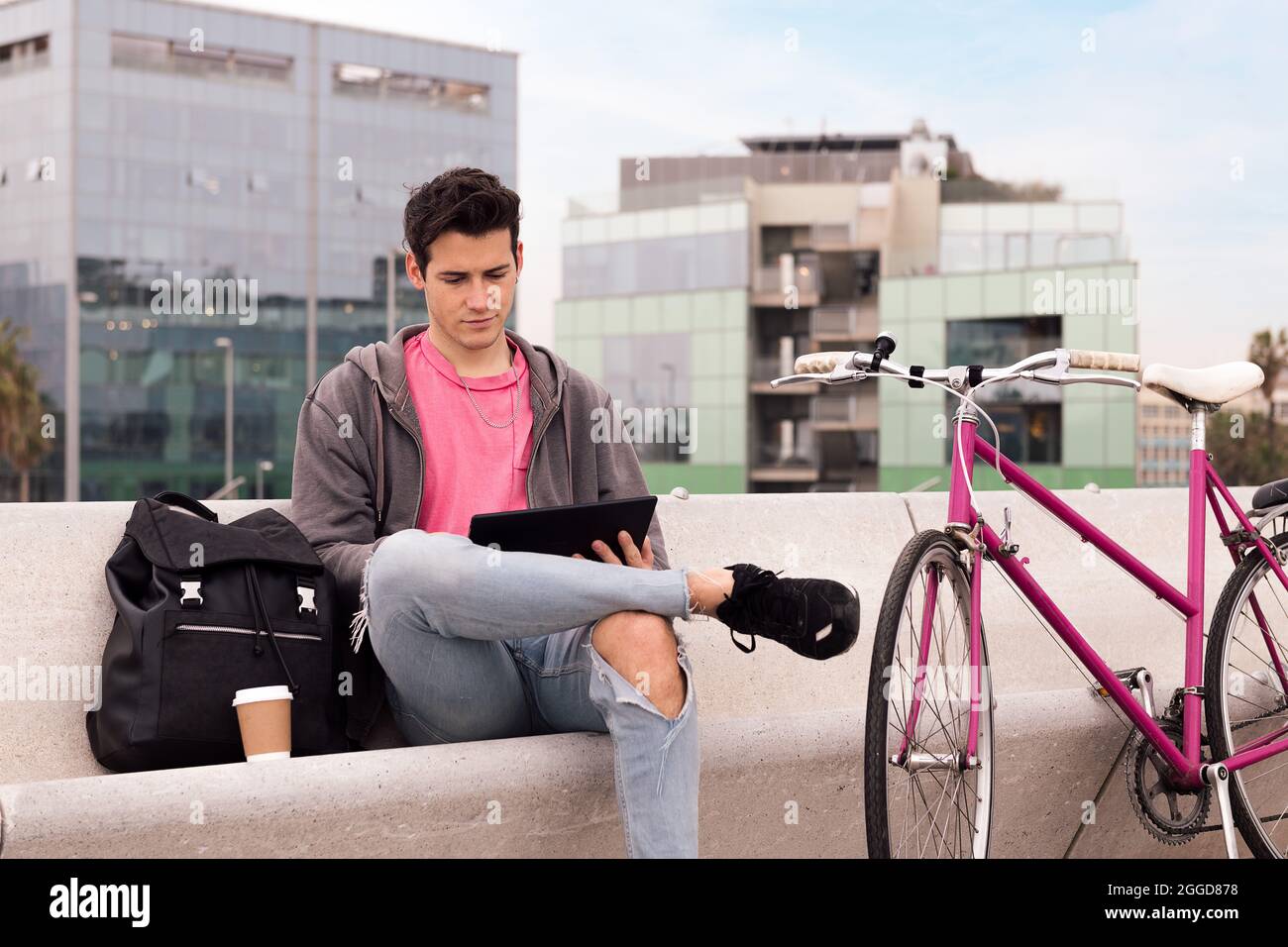 young student sitting outdoors using tablet next to his bicycle, concept of technology and urban lifestyle Stock Photo