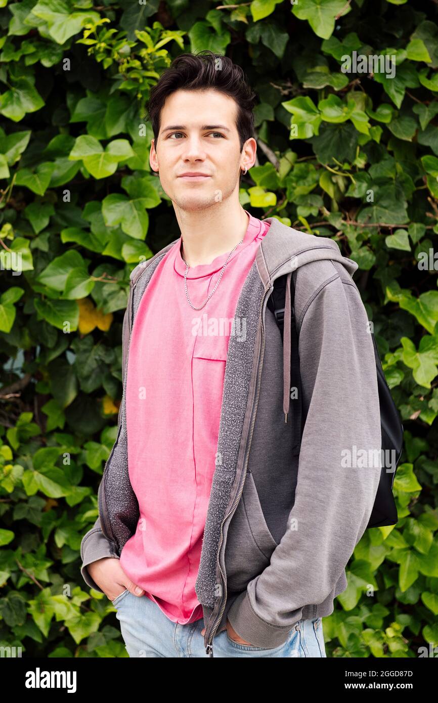 vertical photo of a handsome young man pensive on a green plants background, concept of ecology and teenage lifestyle Stock Photo
