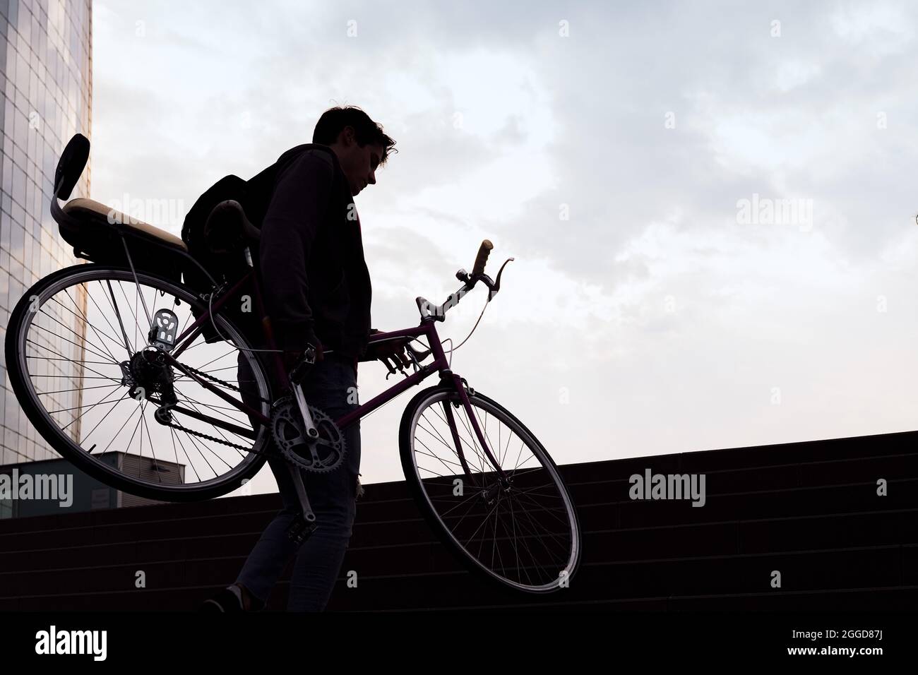 silhouette of a young man carrying bicycle up the stairs, concept of