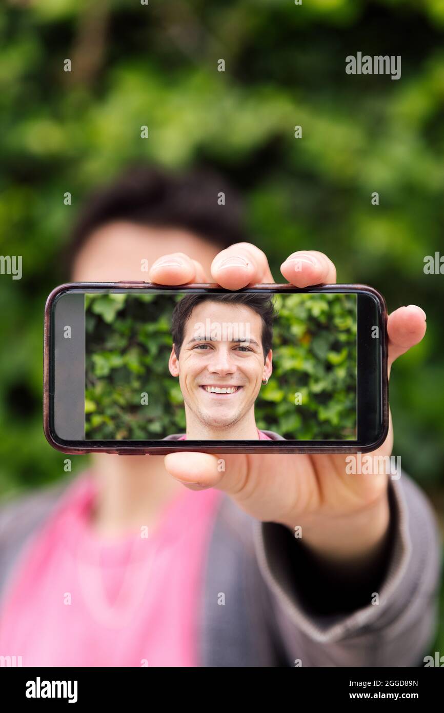vertical photo of a happy young man covering his face with a smart ...