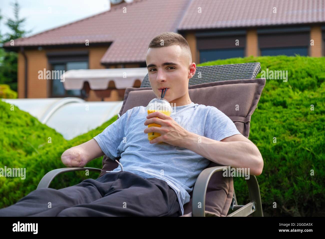 Young man with disability lies on a sun lounger and drinks cocktail  Stock Photo