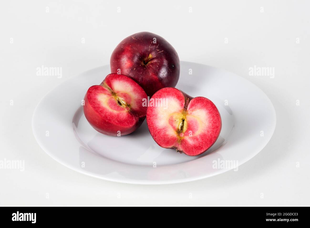 Red fleshed apples on a plate, one sliced to show colour of red flesh inside. Stock Photo