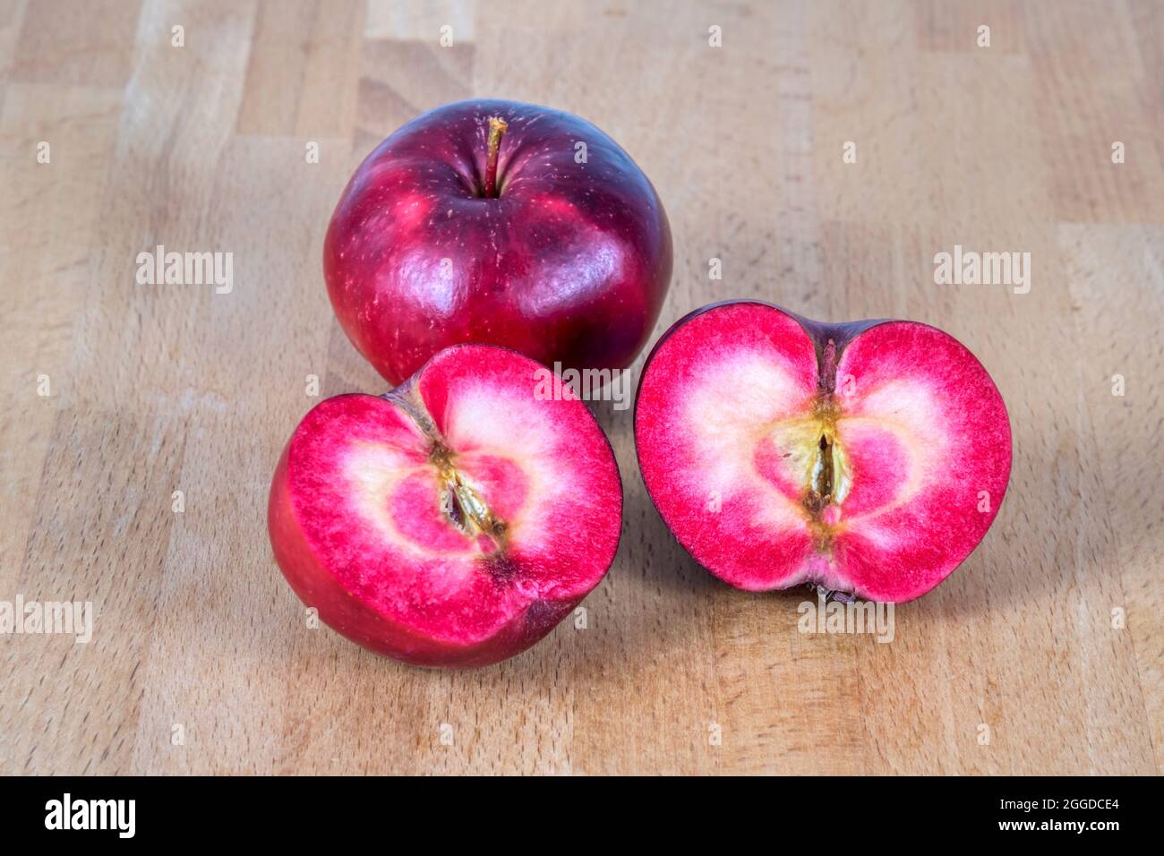 Red fleshed apples on table, one sliced to show colour of red flesh inside. Stock Photo