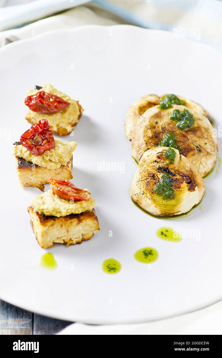 Grilled tempeh with almond cream and sauted mushrooms served with garlic pesto. Stock Photo