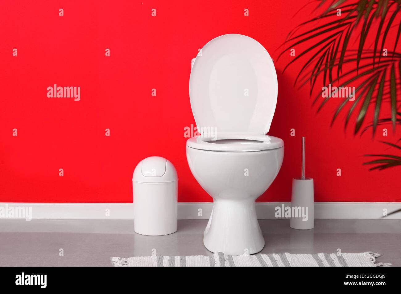 Modern toilet bowl in interior of restroom near red wall Stock Photo