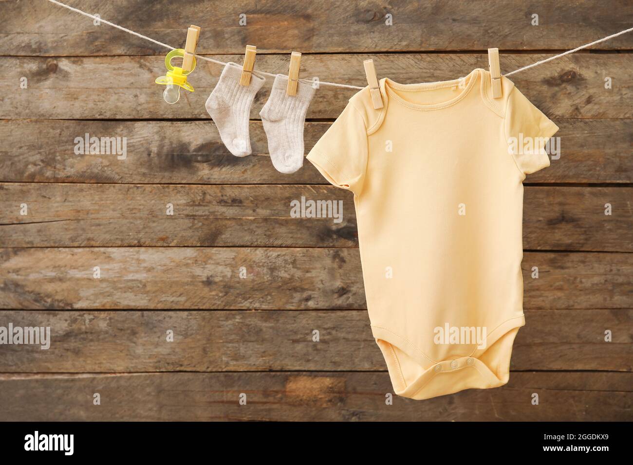 Baby clothes and pacifier hanging on rope against wooden background ...