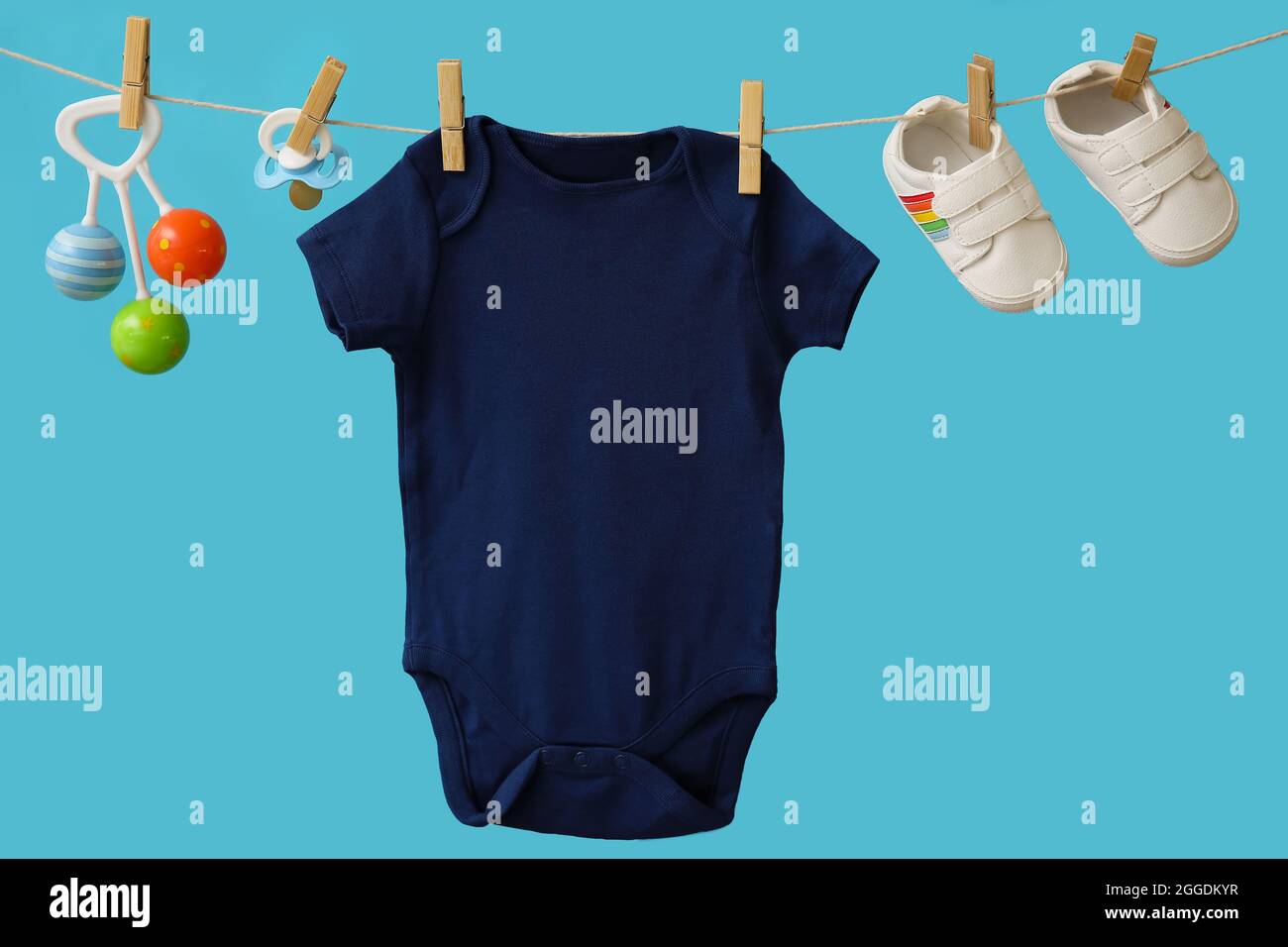Baby clothes, shoes, pacifier and toy hanging on rope against color  background Stock Photo - Alamy