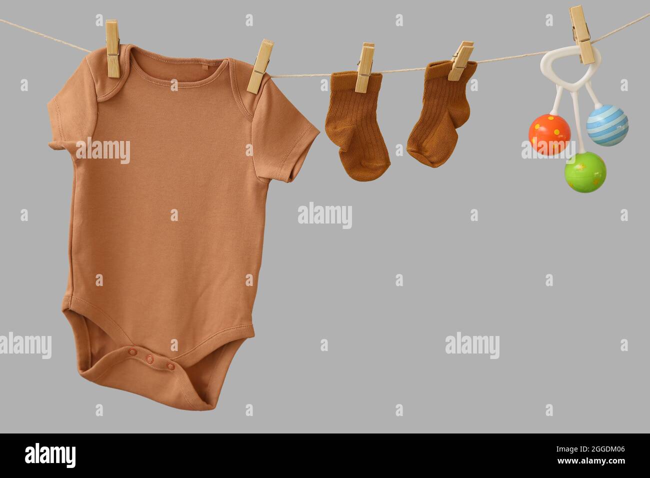 Baby clothes and toy hanging on rope against grey background Stock Photo