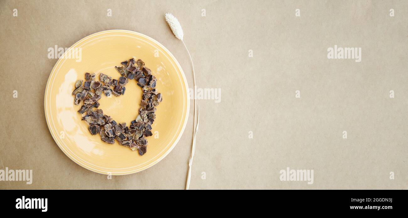 Carob - plant-based alternative - natural product on the plate with dry Lagurus ovatus grass in a shape of heart. Extra wide banner. Organic antioxida Stock Photo