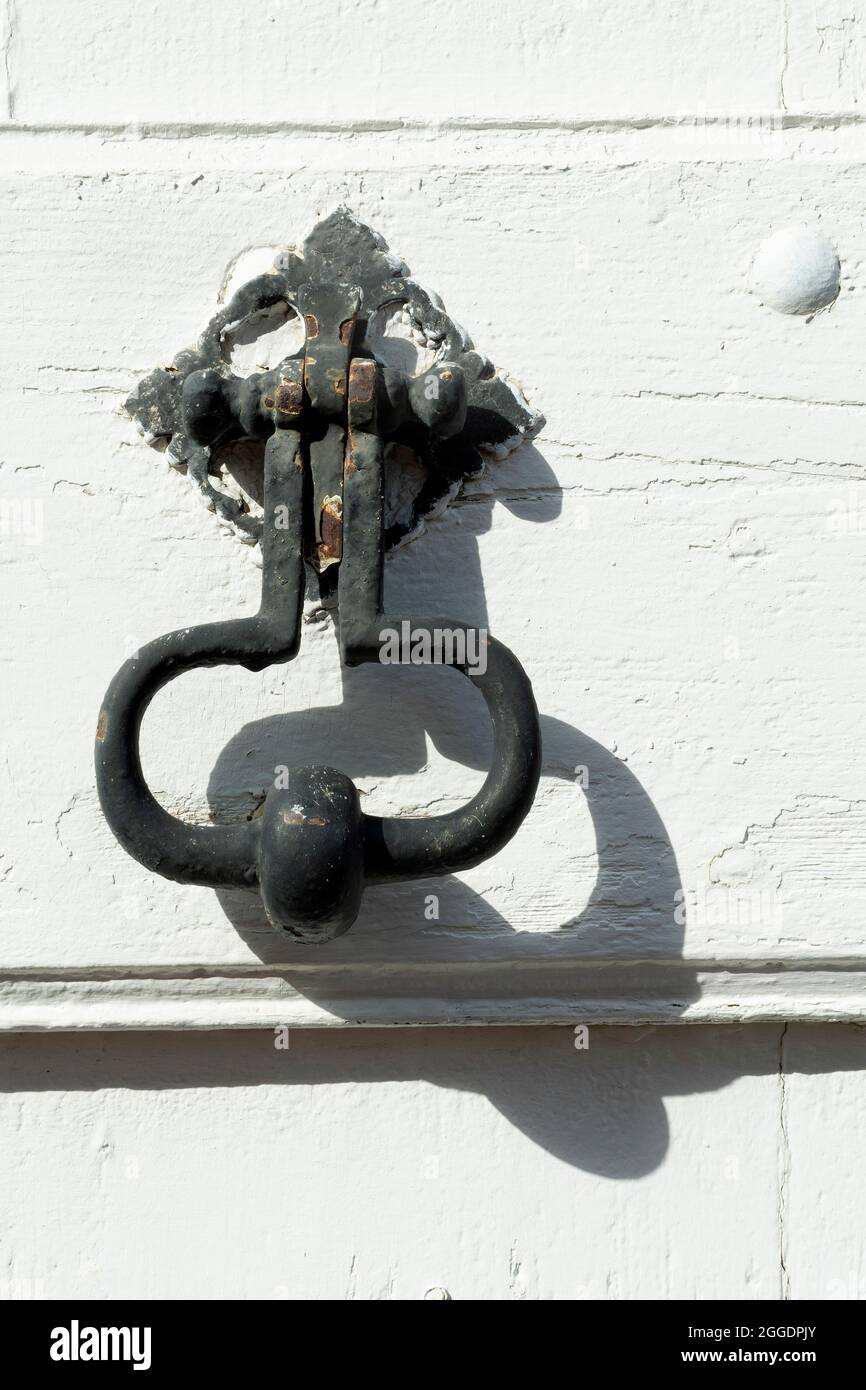 Close-up of an antique door knocker on a weathered white wooden surface showcasing intricate details and unique craftsmanship Stock Photo