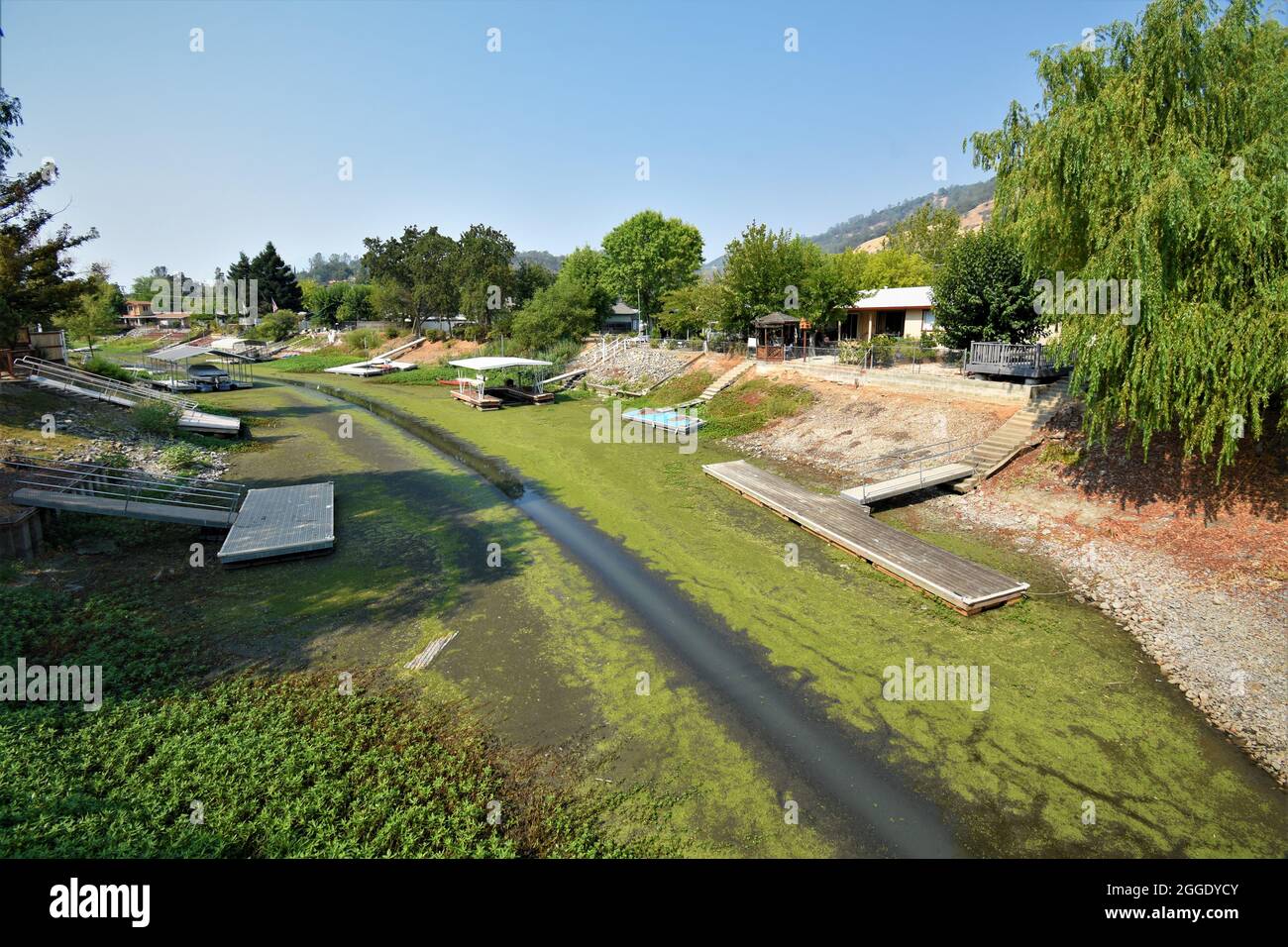 Drought effects in northern California where canal and channel are low or no water and boats are useless & stranded at the docks behind owners  homes Stock Photo