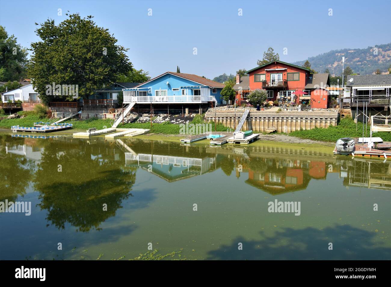 Drought effects in northern California where canal and channel are low or no water and boats are useless & stranded at the docks behind owners  homes Stock Photo