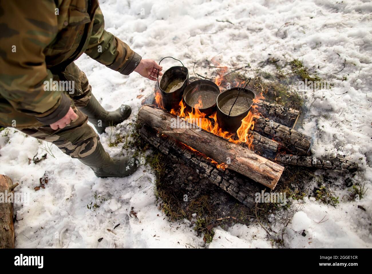 https://c8.alamy.com/comp/2GGE1CR/three-pots-with-boiling-water-on-a-campfire-a-man-in-warm-clothes-is-standing-next-to-him-on-a-winter-day-cooking-on-the-hike-2GGE1CR.jpg