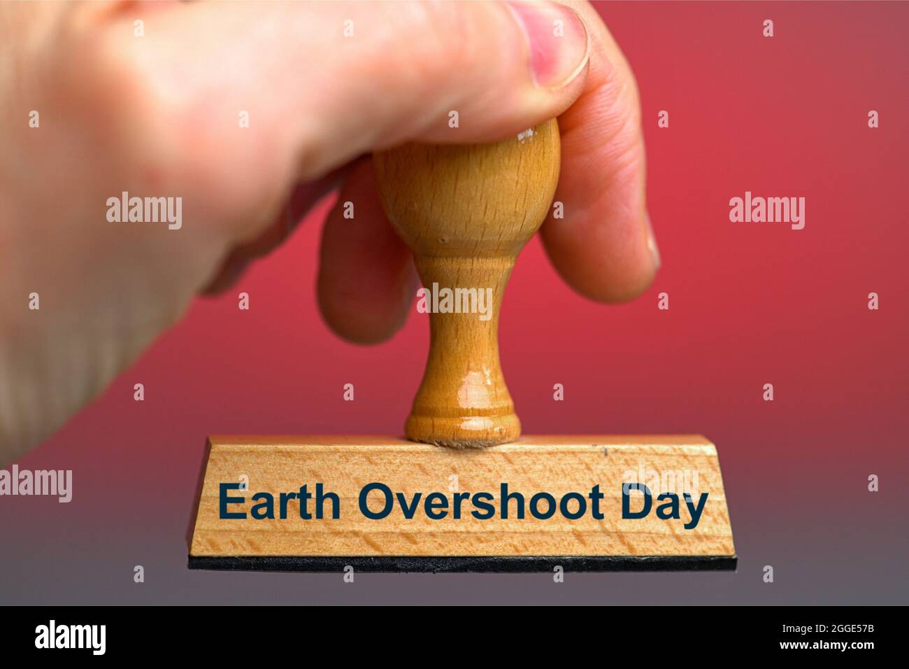 Deutschland. 28th July, 2021. A wooden stamp with the inscription 'Earth Overshoot Day' held by a hand in the bleed. Photo with composing against a red background. The Earth Overshoot Day, also Earth Overload Day, Ecological Debt Day, World Creation Day, World Overload Day or Eco Debt Day, is the day of the current year in an annual campaign by the organization 'Global Footprint Network' on which the human demand for after-growing raw materials the supply and capacity of Earth to reproduce these resources exceeds this year. In 2021, the day falls on July 29th. Credit: dpa/Alamy Live News Stock Photo