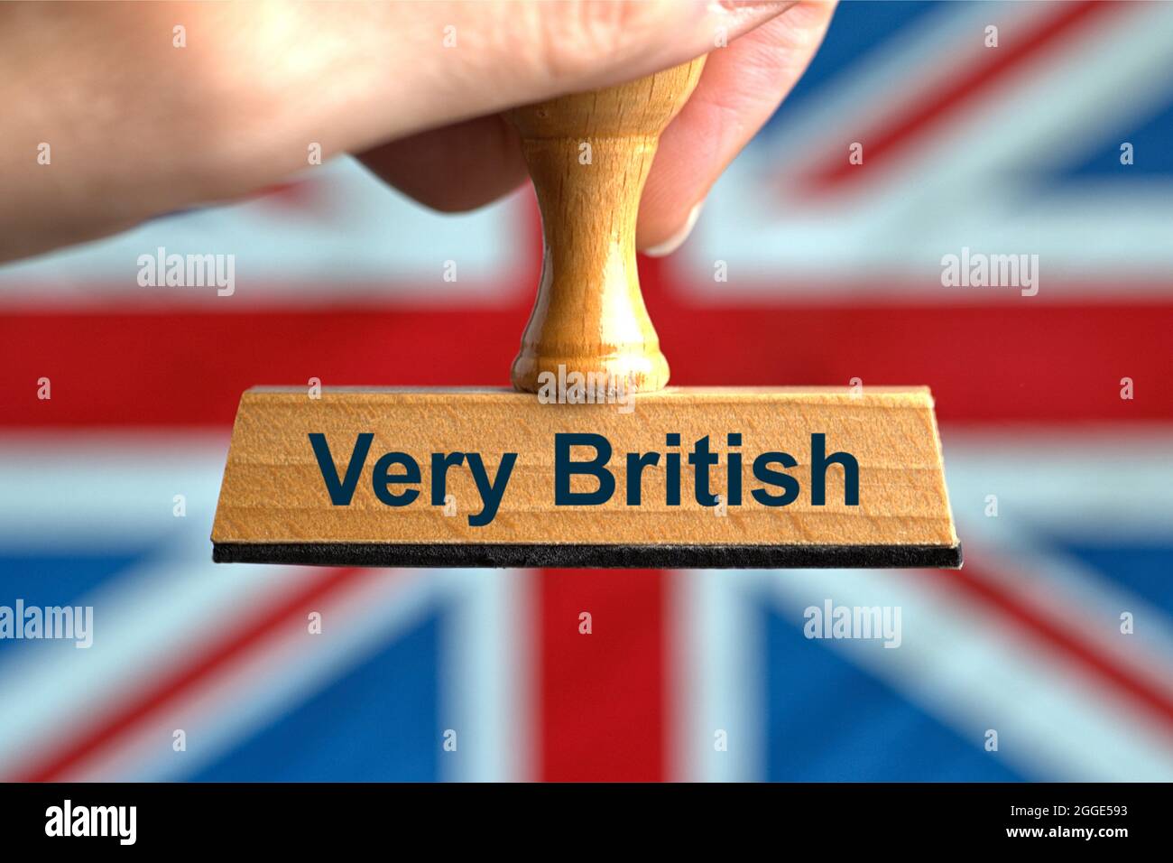 Deutschland. 28th July, 2021. A symbolic wooden stamp with the inscription "Very British", held by a hand in a bleed in front of a blurred flag of Great Britain (GB), the Union Jack in the background. Photo with composing [M]. || Model released Credit: dpa/Alamy Live News Stock Photo
