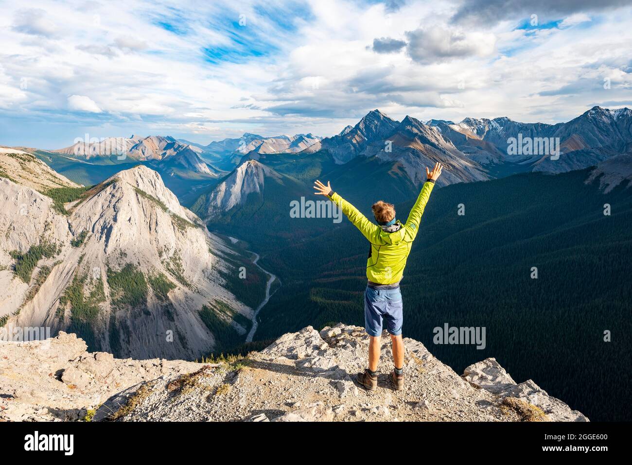 Hiker stretches his arms in the air, mountain landscape with river valley and peaks, peaks with orange sulphur deposits, Overturn Mountain, panoramic Stock Photo