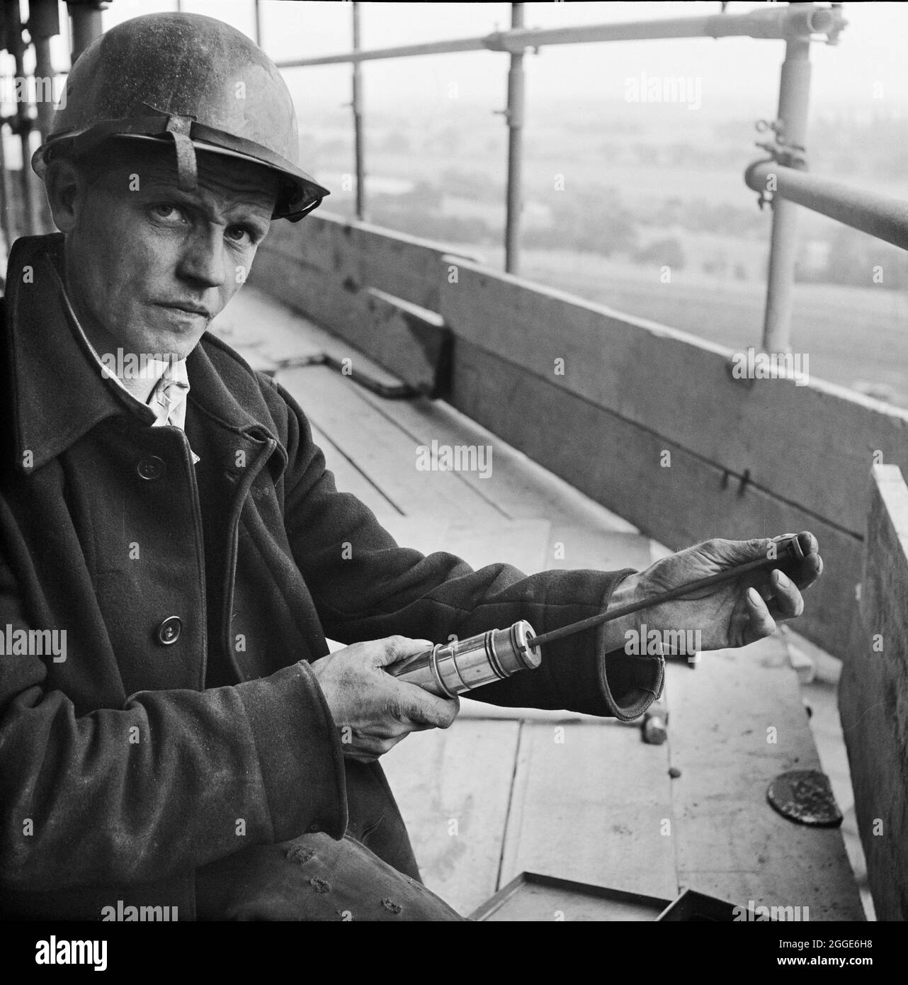 A worker loading a riveting gun during the construction of two sugar silos at Poppleton Sugar Beet Factory. Two sugar silos were built by Laing for the British Sugar Corporation Limited at the Poppleton Sugar Beet Factory. They were designed to hold a total of 16,000 tons of sugar and were the largest to have been built in the country when this photograph was taken. The prestressed post-tensioned concrete silos were made with sliding formwork using hydraulic climbing jacks. Stock Photo