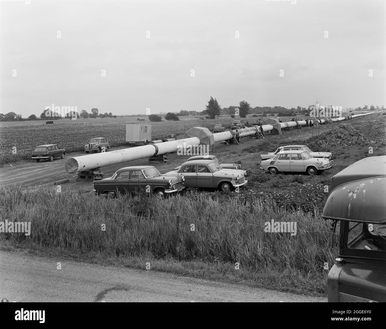 A view of the Fens gas pipeline, showing protective canopies located at joints along the pipe where welding was carried out and workers cars parked alongside the pipeline. Work on laying the Fens gas pipeline started in June 1967 and was a joint venture between Laing Civil Engineering and French companies Entrepose and Grands Travaux de Marseille (GTM) for the Gas Council. Over 600 men worked on the project to lay 36 inch diameter steel pipes starting at West Winch in Norfolk and running to where it linked up with the next contract at Woodcroft Castle in Cambridgeshire. The pipeline crossed fo Stock Photo