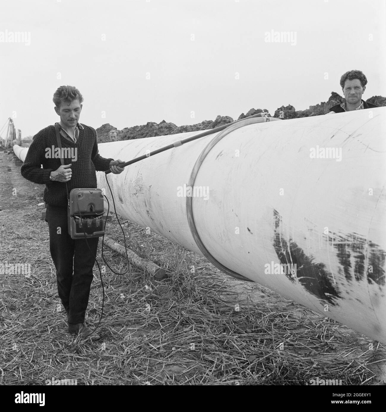 A worker walking along a section of the Fens gas pipeline, operating a holiday detector to check that the pipe is properly sealed with no faults in the wrapping around the pipe. Work on laying the Fens gas pipeline started in June 1967 and was a joint venture between Laing Civil Engineering and French companies Entrepose and Grands Travaux de Marseille (GTM) for the Gas Council. Over 600 men worked on the project to lay 36 inch diameter steel pipes starting at West Winch in Norfolk and running to where it linked up with the next contract at Woodcroft Castle in Cambridgeshire. The pipeline cros Stock Photo