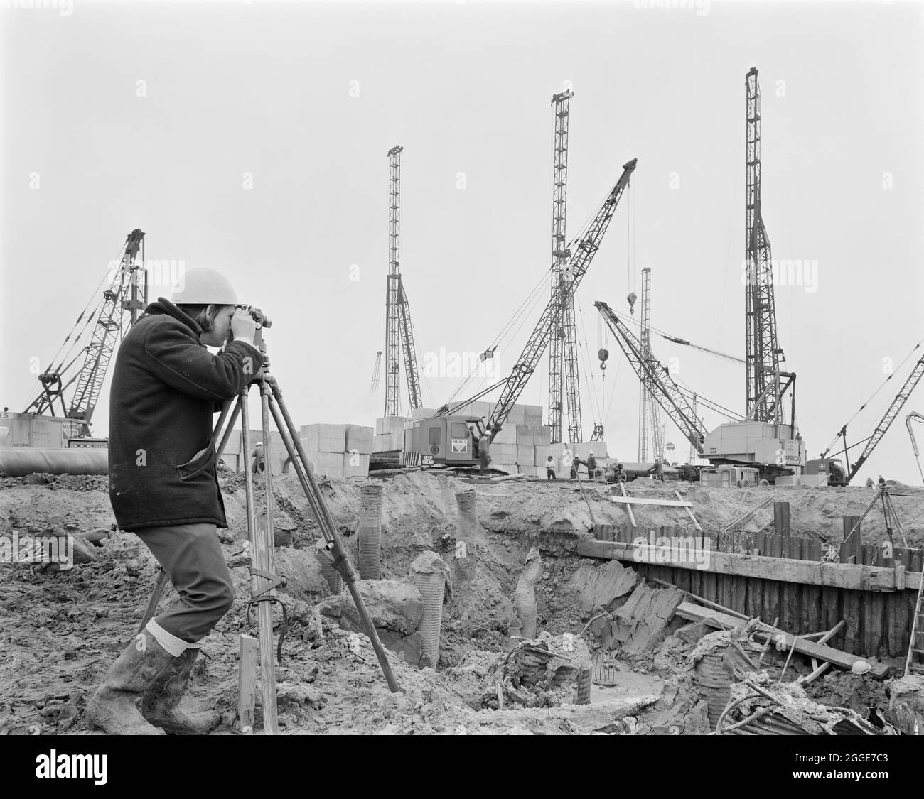A Laing surveyor using a theodolite on the construction site of the Isle of Grain Power Station. The Isle of Grain Power Station was an oil fired power station built in the 1970&#x2019;s by multiple contractors, including John Laing and Son Ltd. When the power station opened in 1979, it had the second tallest chimney in the UK at 244 metres high. The power station has now been demolished and the chimney was destroyed in September 2016. A new Combined Cycle Gas Turbine (CCGT) power station has been built at the site. Stock Photo