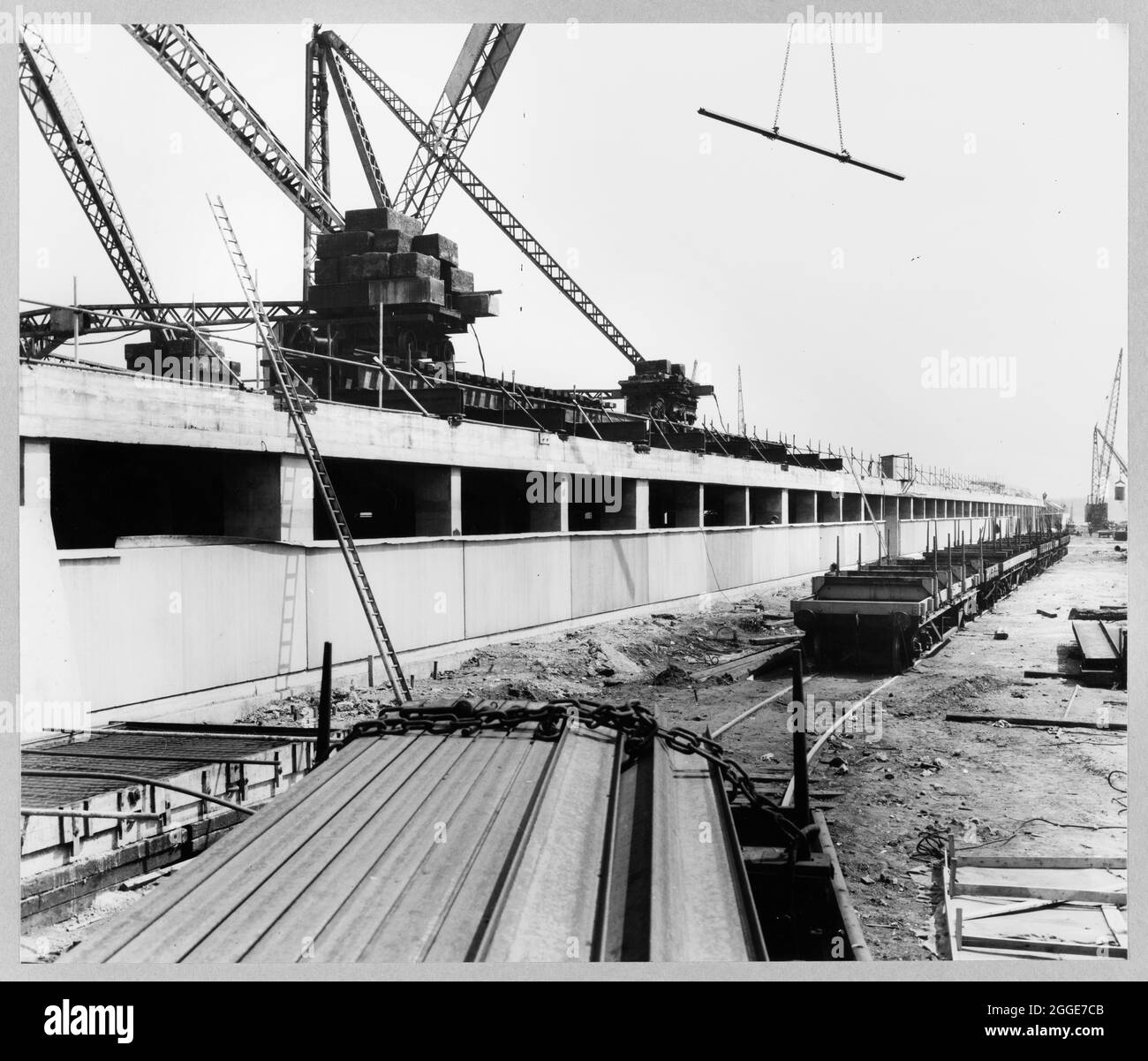A view of the new foundry under construction at the Ford Motor Company Works, showing cladding panels being erected on part of the south elevation, and freight wagons on a rail track in the foreground with cranes working overhead. This image was catalogued as part of the Breaking New Ground Project in partnership with the John Laing Charitable Trust in 2019-20. Stock Photo