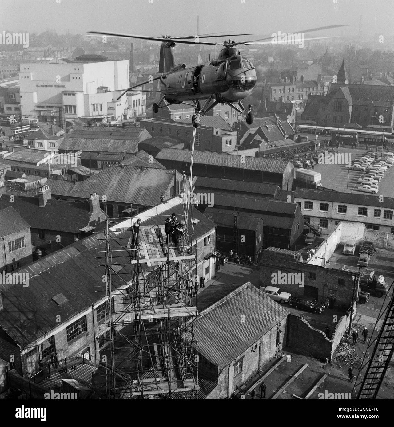 A view looking north from the roof of Coventry Cathedral, showing a RAF Belvedere helicopter attempting to hoist the 80ft bronze spire for the new cathedral from a scaffolding tower on site, with the city of Coventry in the background including the bus station and The Coventry Theatre. The photograph was taken during 'Operation Rich Man' a joint project involving Royal Air Force staff and Laing staff. This involved a RAF Belvedere helicopter hoisting in to place the 80ft bronze spire on to the new cathedral. The part of the operation to lower the 1/2 ton cross that sits on top of the spire had Stock Photo