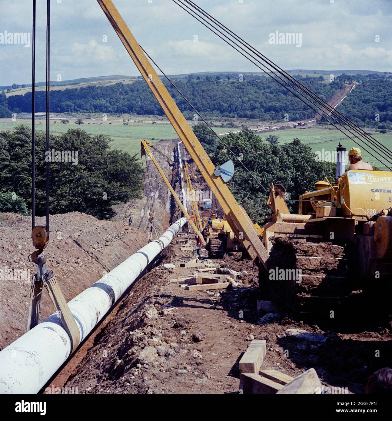 A view along the route of the Brampton pipeline, showing pipelaying equipment in the foreground lowering the pipeline into a trench. In 1975, Laing Pipelines laid the Brampton gas pipeline between Longtown near Carlisle to the east of Bishop Auckland. The pipeline is a section of the Frigg pipeline carrying natural gas from the North Sea to near Peterhead in Scotland. The headquarters for the Laing contract was located at an old quarry near Brampton. Stock Photo