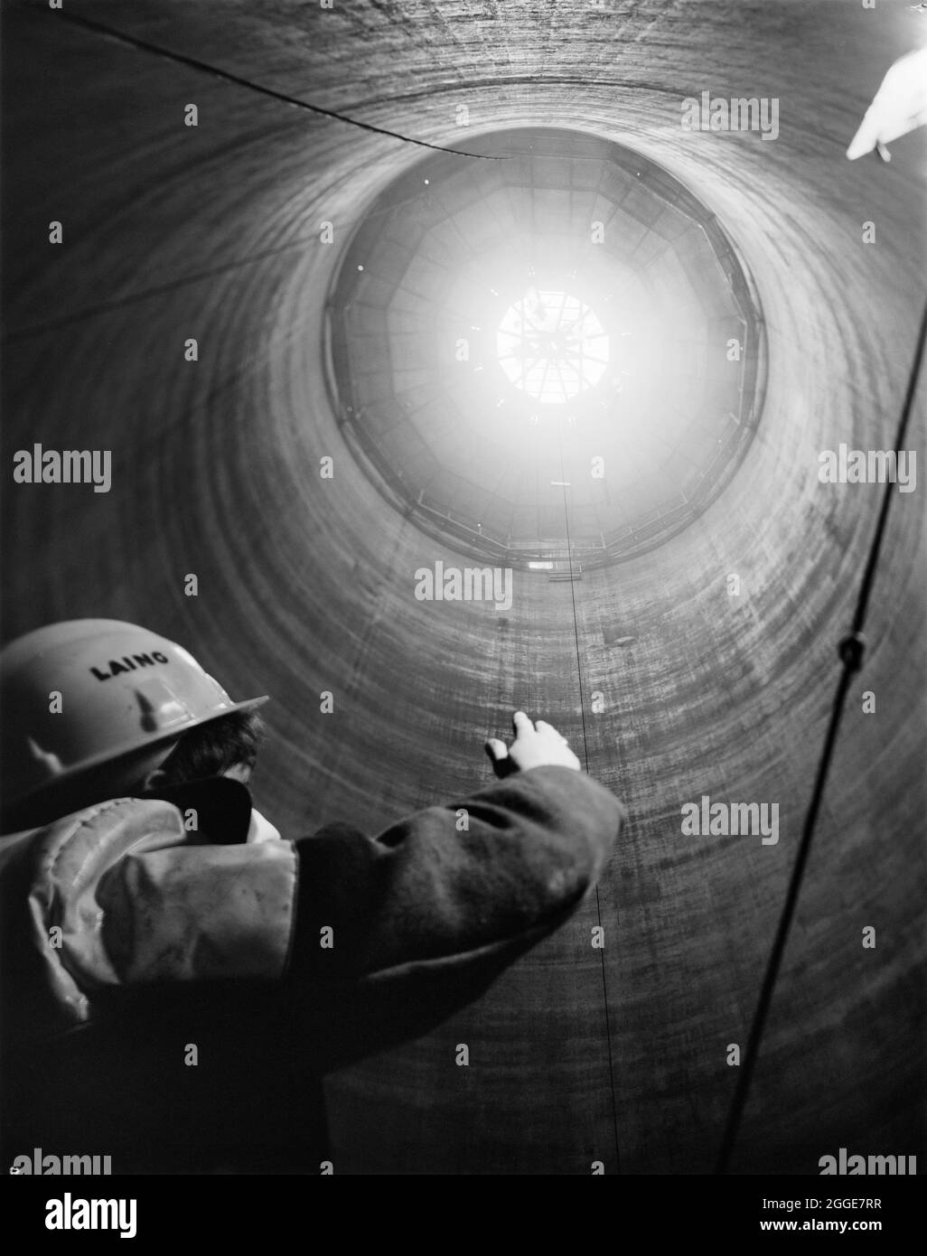 An interior view looking up towards the partially completed conical roof of a sugar silo at Felsted Beet Sugar Factory, with a Laing employee gesturing towards the roof. A sugar factory was built near Felsted in 1926. The first silo to be built by Laing at Felsted Beet Sugar Factory was constructed in 1956 and took three weeks; the second silo was built in six days in 1974. The factory produced sugar until 1981 and the site was then used for storage until 1991. It was later redeveloped for housing. This photograph was published in the April 1974 edition of 'Team Spirit', the Laing newsletter. Stock Photo