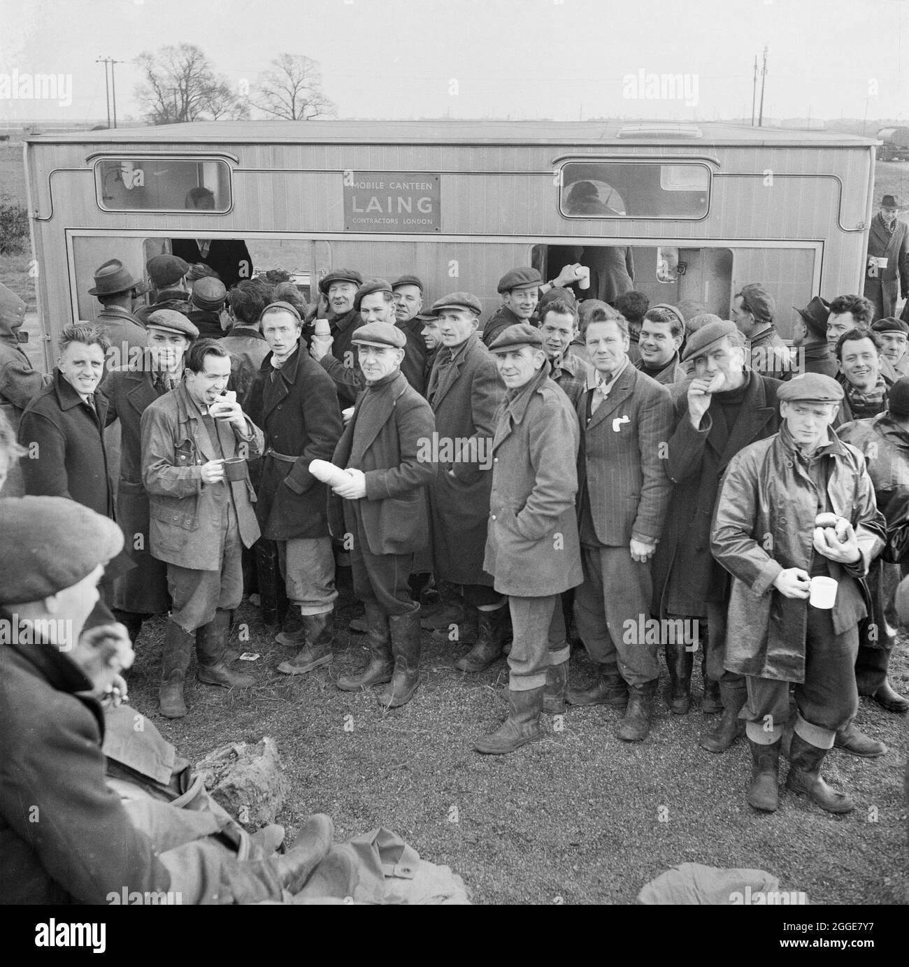 A large group of Laing workers using a mobile canteen following severe flooding on the construction site of Coryton Oil Refinery. On the night of Saturday 31st January through to the morning of Sunday 1st February 1953, severe floods struck parts of the UK, Scotland, Belgium and the Netherlands. The natural disaster is often referred to as the North Sea Flood of 1953. Severe flooding occurred along the east coast of the UK. The site of Coryton Oil Refinery flooded as the river wall protecting the site was breached in 14 places. An article detailing the disaster and subsequent recovery operatio Stock Photo