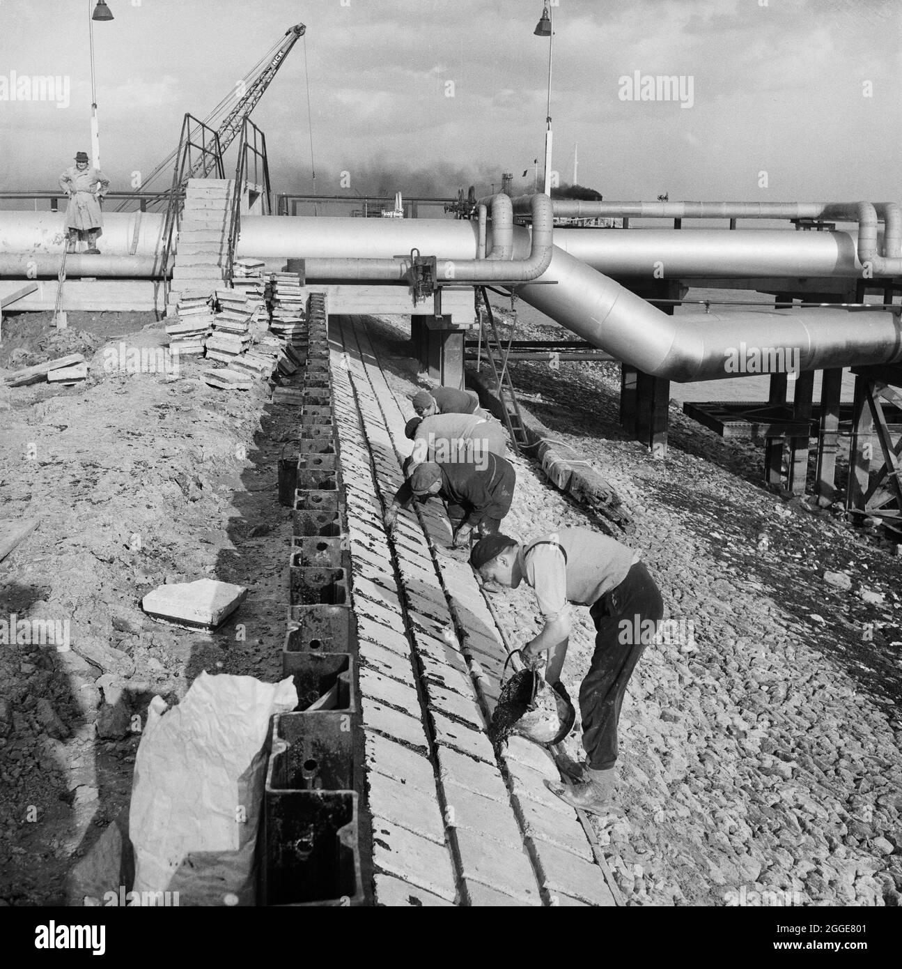 Workers constructing a protective wall of precast concrete blocks at Coryton Oil Refinery, as part of extensive flood prevention work at the site. On the night of Saturday 31st January through to the morning of Sunday 1st February 1953, severe floods struck parts of the UK, Scotland, Belgium and the Netherlands. The natural disaster is often referred to as the North Sea Flood of 1953. Severe flooding occurred along the east coast of the UK. The site of Coryton Oil Refinery flooded as the river wall protecting the site was breached in 14 places. An article detailing the disaster and subsequent Stock Photo
