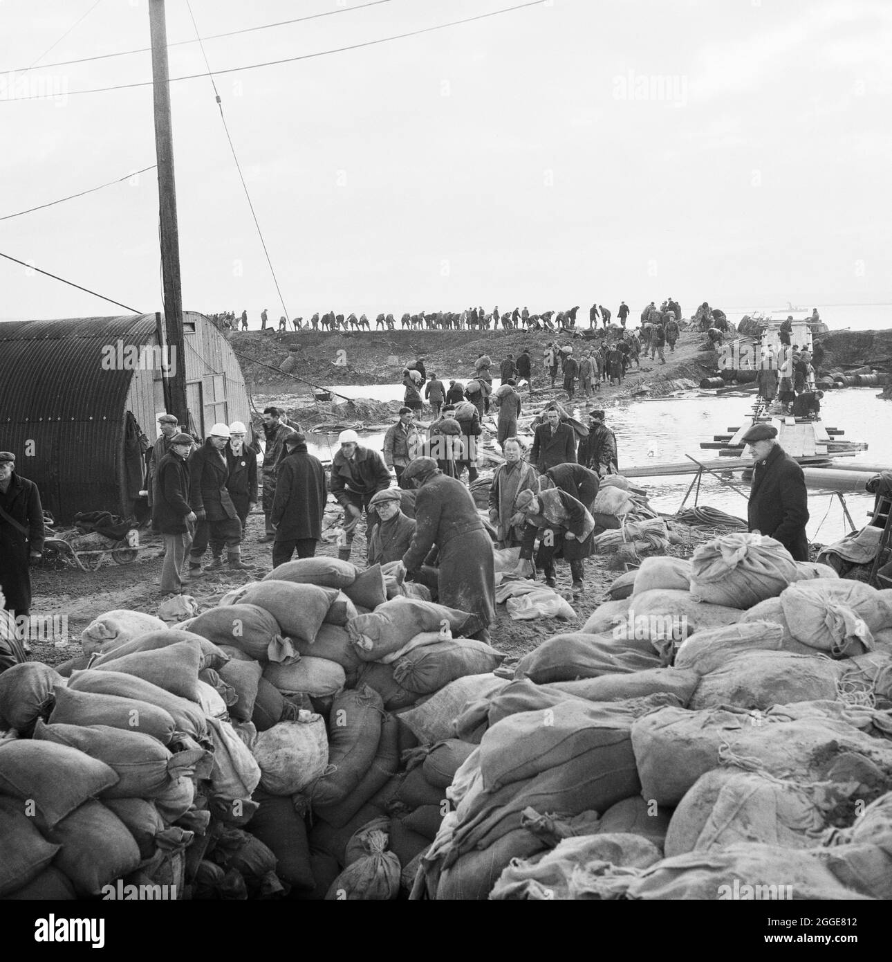 Laing workers collecting and transporting sandbags to repair breaches in the river wall after flooding on the construction site of Coryton Oil Refinery. On the night of Saturday 31st January through to the morning of Sunday 1st February 1953, severe floods struck parts of the UK, Scotland, Belgium and the Netherlands. The natural disaster is often referred to as the North Sea Flood of 1953. Severe flooding occurred along the east coast of the UK. The site of Coryton Oil Refinery flooded as the river wall protecting the site was breached in 14 places. An article detailing the disaster and subse Stock Photo