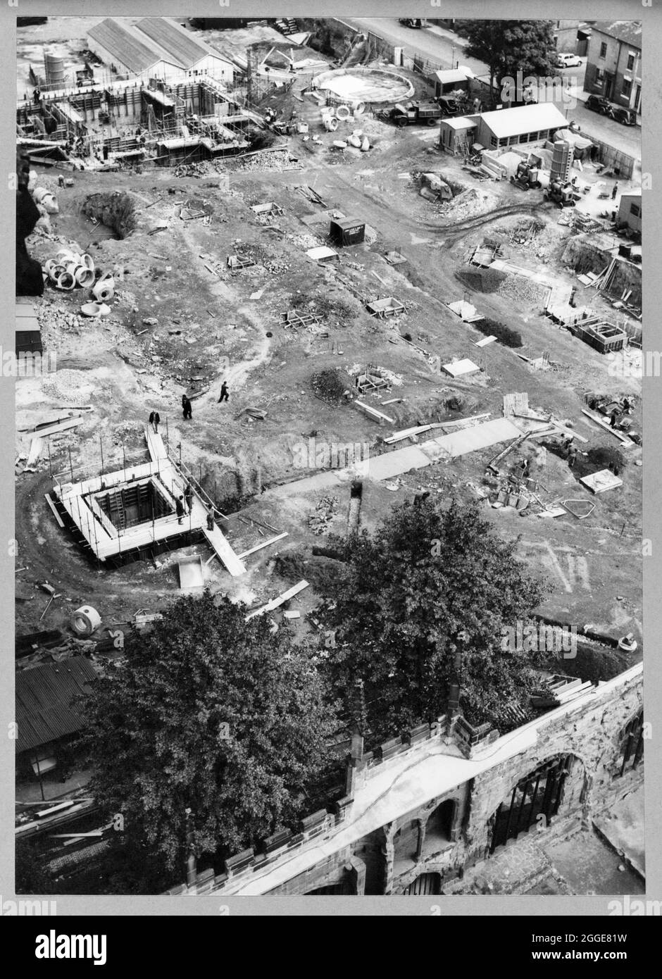 A view of the construction site of Coventry Cathedral taken from the spire of the old Coventry Cathedral, looking down on the original graveyard and the remains of the Old Priory Row which traversed the site from east to west. The photograph shows the construction of the new Coventry Cathedral, designed by Basil Spence in 1951 and constructed between the mid-1950s and 1962. It replaced the ruined Cathedral Church of St Michael which had been badly damaged by bombing in 1941. The caption below the photograph in the album reads &quot;... In the centre of the middle ground can be seen the constru Stock Photo