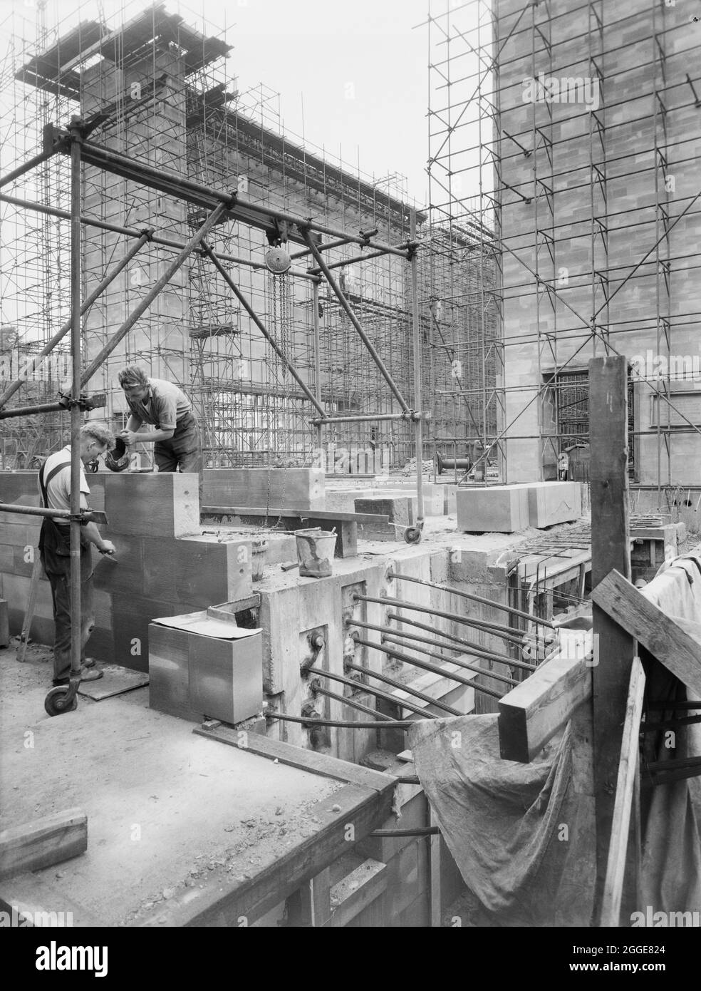 A view of the construction site at Coventry Cathedral, showing two builders constructing a wall in the foreground and scaffolding erected around the shell of the building in the background. This image was catalogued as part of the Breaking New Ground Project in partnership with the John Laing Charitable Trust in 2019-20. Stock Photo