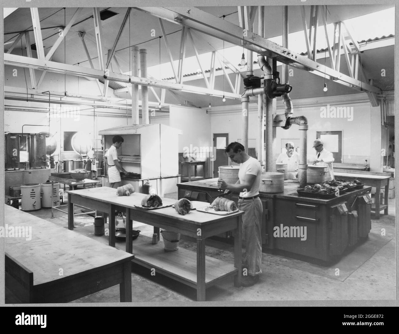 The kitchen of the Balfour Beatty camp on the Berkeley Nuclear Power Station construction site with four men cooking and preparing food for the workers. This image was catalogued as part of the Breaking New Ground Project in partnership with the John Laing Charitable Trust in 2019-20. Stock Photo