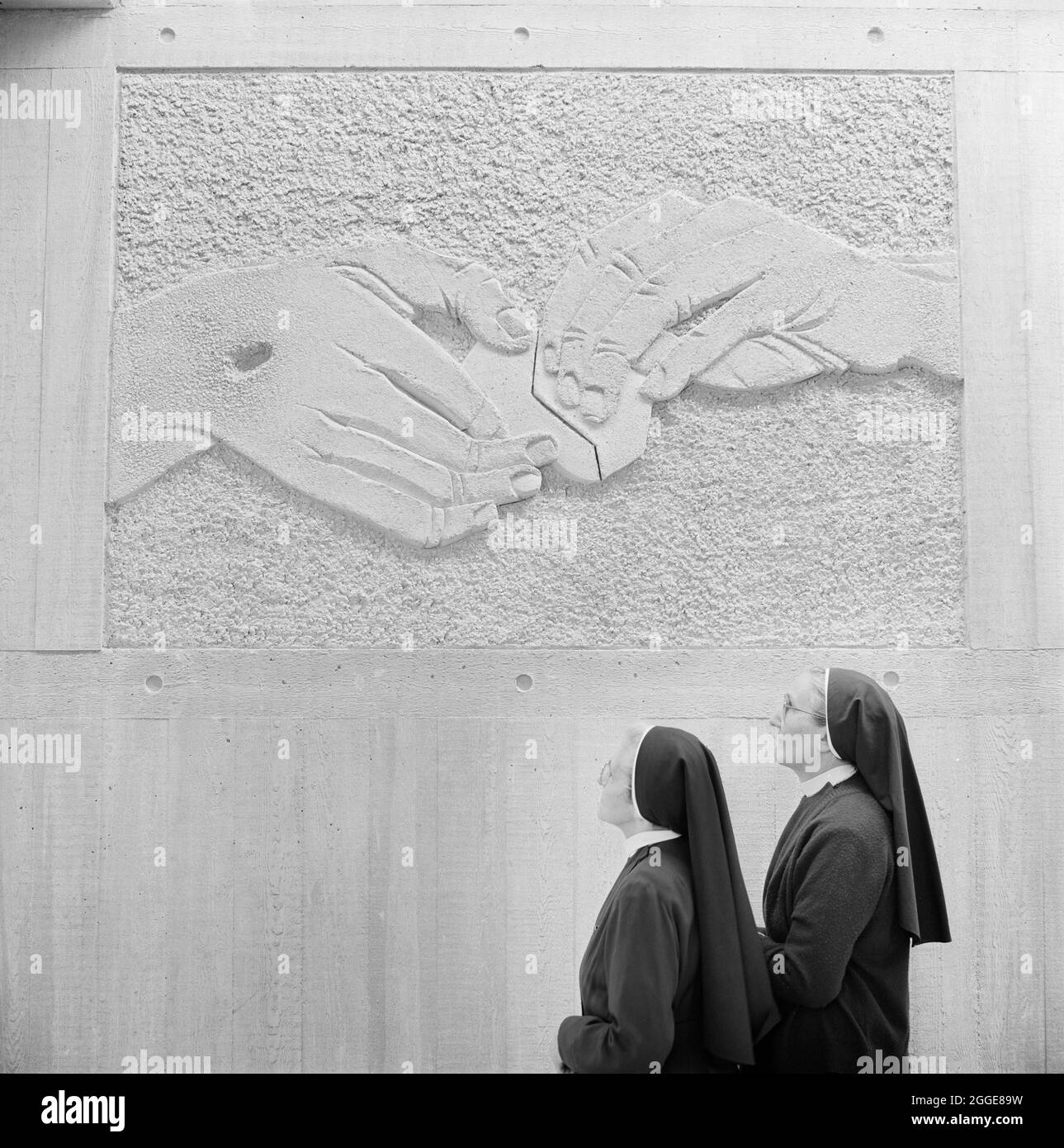 Two nuns looking up at a panel created in Faircrete by sculptor William Mitchell in Clifton Cathedral, depicting one of the Stations of the Cross. This Roman Catholic Cathedral was designed by Ronald Weeks, E S Jennett and Antoni Poremba of the Percy Thomas Partnership. It was built by John Laing &amp; Son Limited between 1969-1973 and was constructed using pre-cast concrete panels and in-situ concrete. In 1974 it received the Concrete Award from the Concrete Society. The English sculptor William Mitchell (born 1925) was commissioned to create 14 panels showing the Stations of the Cross, depic Stock Photo