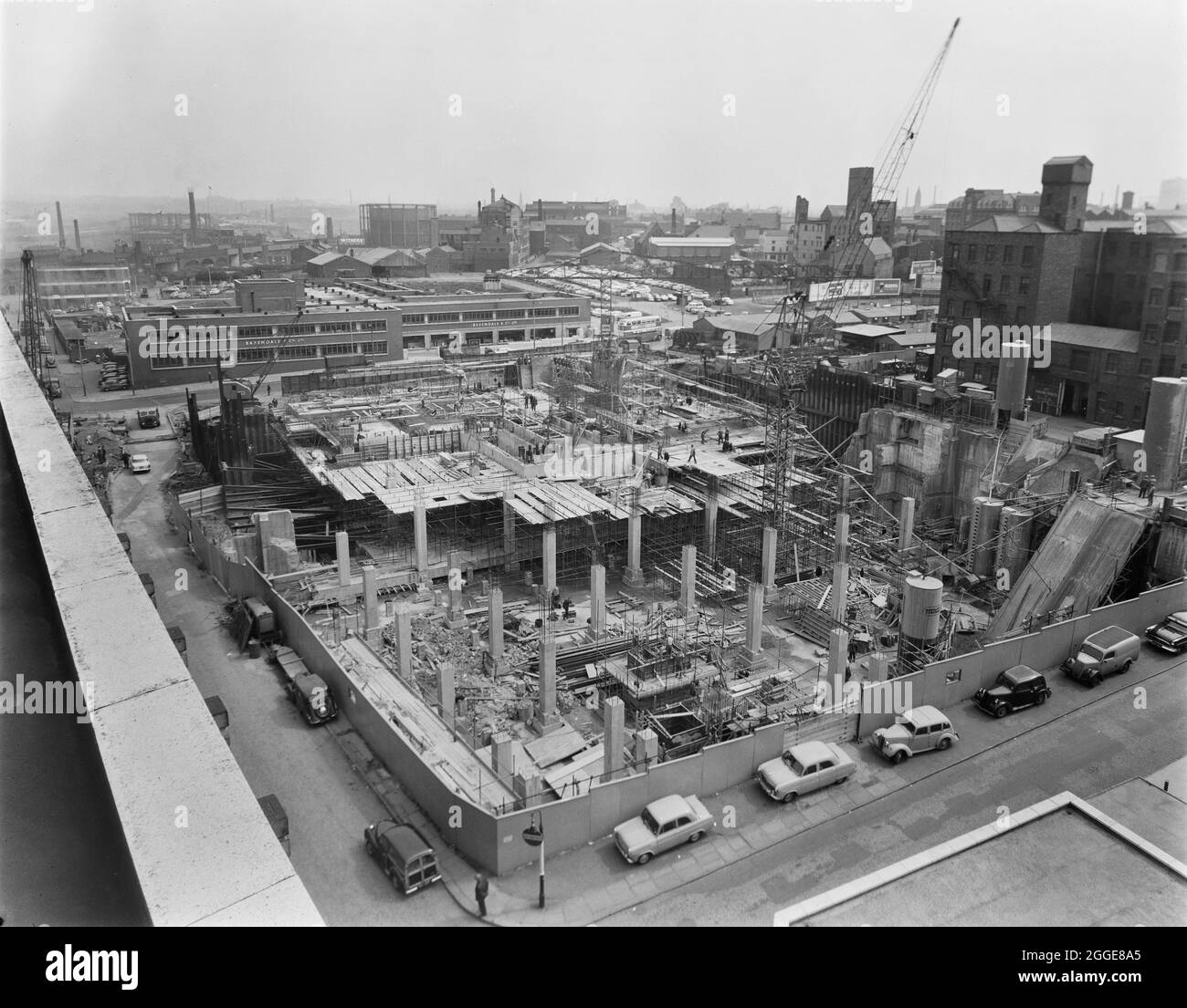 A view from the roof of the Co-operative Society Building on Dantzic Street, looking north-east over the construction site for the Co-operative Insurance Society (CIS) Building, showing the construction of the ground floor slab over the deep basement section. The caption beneath the corresponding print of this image reads: &quot;Foreground columns ready to receive floor slab were built off an existing air raid shelter roof. Weitz G60 and Buildmaster Tower Cranes are in use over the deep basement and shelter roof sections respectively. Concrete mixing plant can be seen in the right of the photo Stock Photo